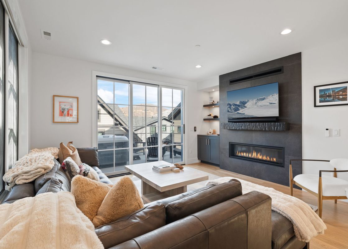 Modern living room at Snowbound at Kings Crown with a leather sectional, sleek fireplace, TV, and glass doors leading to a balcony with a hot tub.
