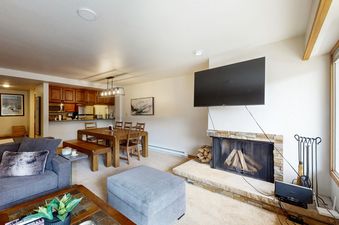 A welcoming living room and dining area in Fallridge 204 with a gray sofa, a wooden dining table, and a stone fireplace.