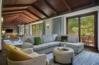 A spacious Montage Flagstaff Suite living area with a large grey sectional sofa, an ottoman, and an armchair, facing large windows with an exterior view of a lush green hillside.