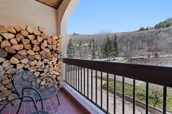 The private balcony of The Charter F3305 features a large stack of firewood next to two metal chairs, with a mountain view in the background.