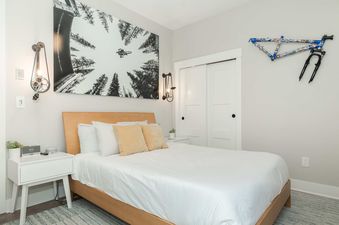A king bedroom at Starview Chalet featuring a king-sized bed with white sheets and golden pillows, flanked by industrial-style sconces and modern nightstands, with a large black and white art piece above the bed.