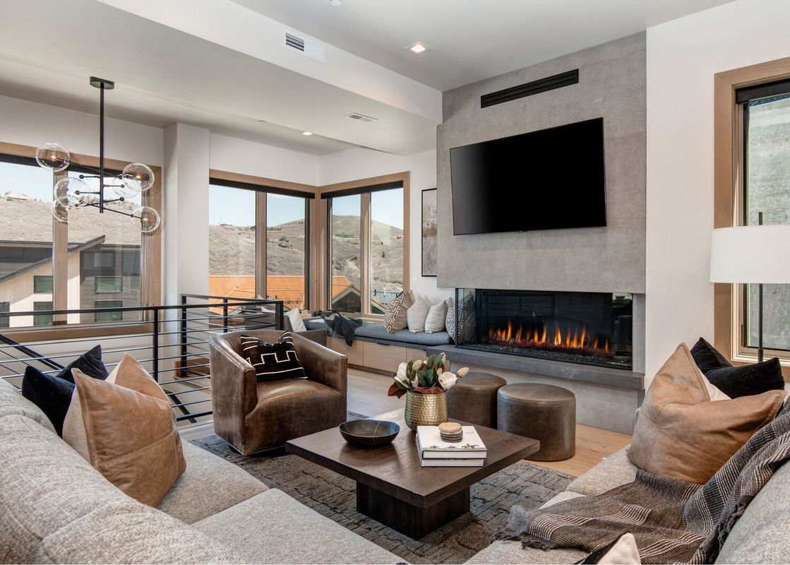 The living area at Abode at Powder King features a large sectional sofa, a fireplace with a TV mounted above, and expansive windows offering mountain views.