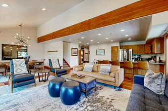 The open concept living area at Silver Cliff Village 205 features a tan leather sofa, a blue sofa, and a modern dining area with a unique chandelier.