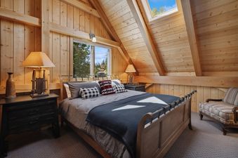 A cozy bedroom at Rested Ridge Ski Haus with a bed, wooden nightstands, and a window with an exterior view of trees.
