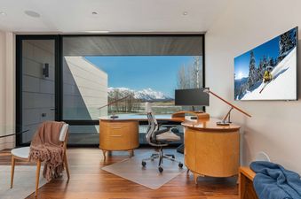 Modern home office at The Dragonfly Lodge with a curved wooden desk and a large window looking out at snow-capped mountains.