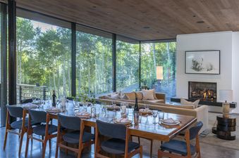 A modern dining room with a large window overlooking a forest.