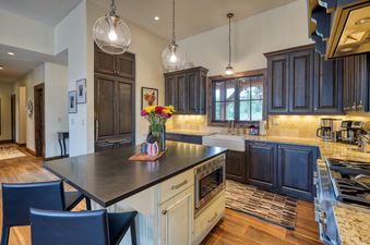 A modern kitchen with dark wood cabinets, granite countertops, and a central island with bar stools and a built-in microwave.