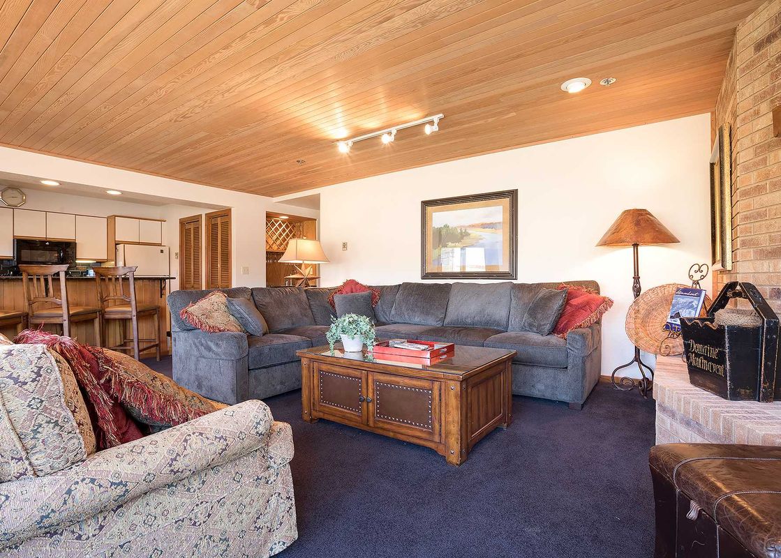 A cozy living area at Chateau Chamonix CX134 with a gray sectional sofa, a wooden coffee table, and a wood-paneled ceiling.