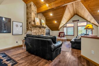 The living area of Ski House on Lowell has a stone fireplace, black leather couches, and a large window offering a view of the mountains.