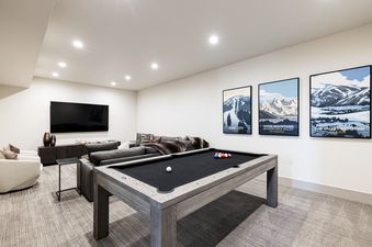 A spacious game room at Frostwood Links features a billiards table, a comfortable L-shaped sectional sofa, and a large flat-screen TV.