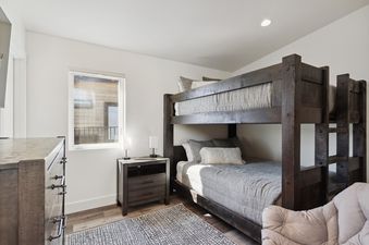 The bunk bed bedroom at Quarry A21, featuring a dark wood bunk bed with grey bedding, a nightstand with lamps, a dresser, and a window.