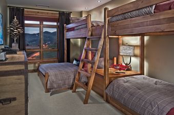 A cozy bedroom with wooden bunk beds, plaid bedding, and a large window offering a view of mountains.