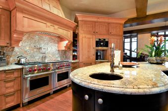 A luxurious kitchen with wooden cabinetry, granite countertops, a professional-grade stove, and a kitchen island with a built-in sink.