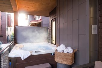 An outdoor hot tub with steaming water is surrounded by fresh white towels in a wicker basket on a modern balcony.