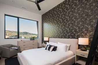 A serene bedroom at Aria Ridge with a large window overlooking a mountainous landscape, a comfortable bed, and stylish decor.
