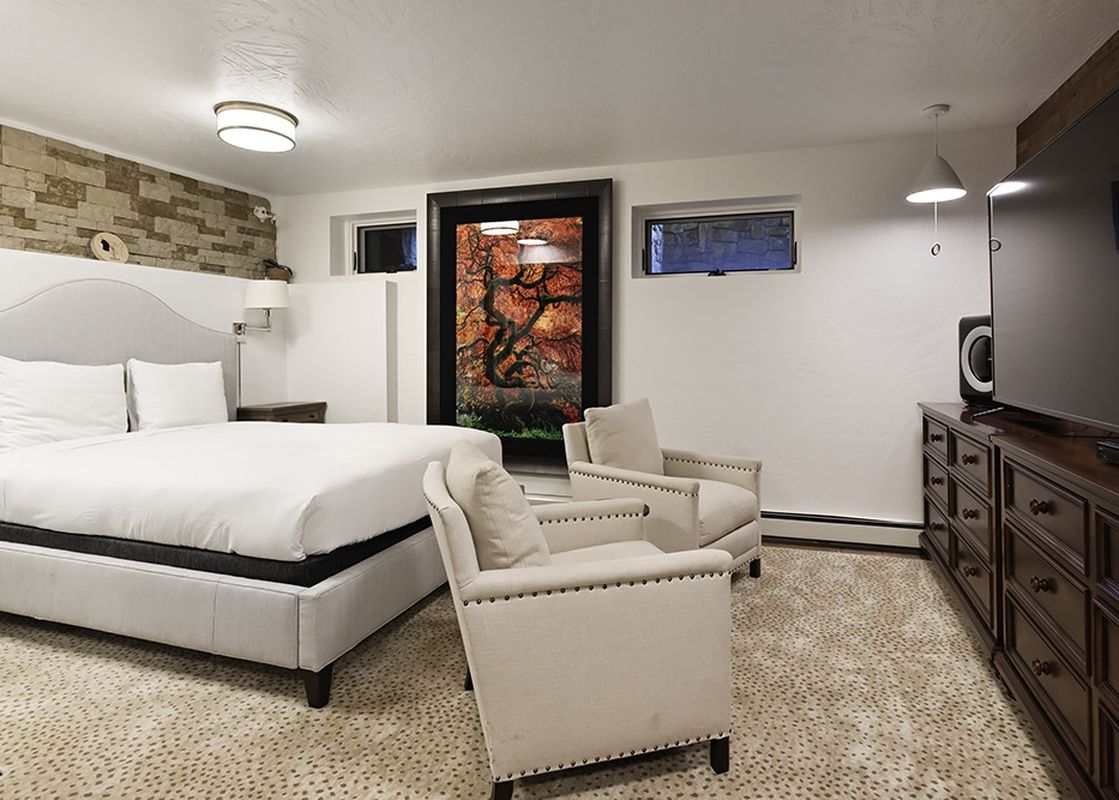 A spacious bedroom features a large bed with white linens, two comfortable armchairs, and a TV dresser.