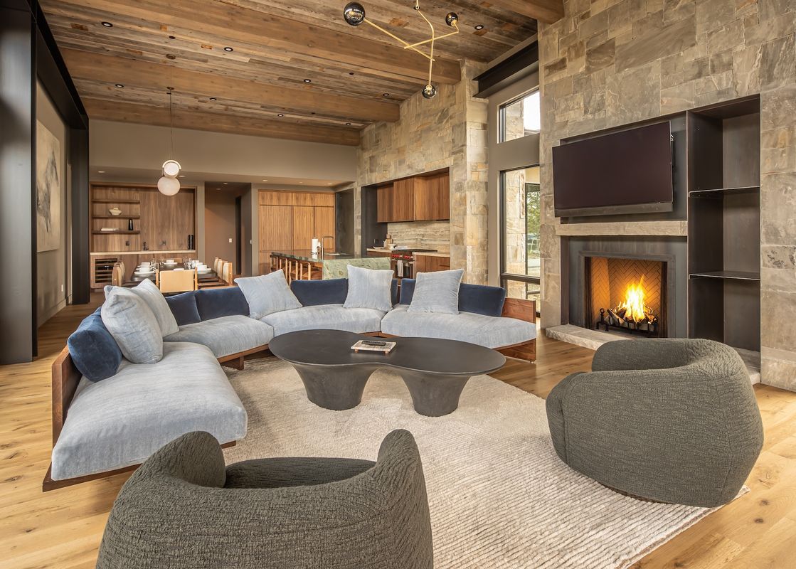 The contemporary living space at Little Thunder Chalet features an open layout, a comfortable sectional sofa, and a striking stone fireplace, creating an inviting and luxurious atmosphere.