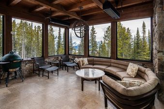 7 Renegade Rd Moonlight Basin Lodging features an expansive covered patio with panoramic views of the mountains, a gas grill, comfortable seating, and a cozy sectional sofa.