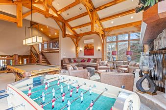 A large living room featuring a foosball table, a pool table, and a comfortable seating area with an L-shaped sofa and armchairs.