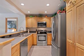 The kitchen at St James Place 325 features light wood cabinetry, stainless steel appliances including a refrigerator, microwave, oven, and dishwasher, and a gray countertop with a double sink and a faucet.