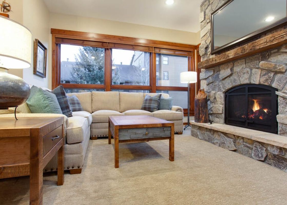 Cozy living room in Kutuk 212 with a stone fireplace, beige sectional sofa, and wooden furniture.