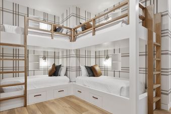 The image shows a cozy bedroom with multiple white bunk beds featuring wooden ladders and railings, set against a plaid patterned wallpaper.