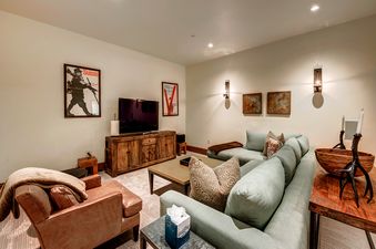 A cozy living room with a large sectional sofa, a coffee table, a TV, and a leather armchair.