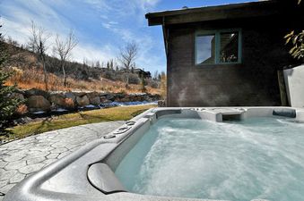 A close-up view of the outdoor hot tub at Solamere Home, showing bubbling water and steam rising against a backdrop of a modern house exterior and a scenic hillside.