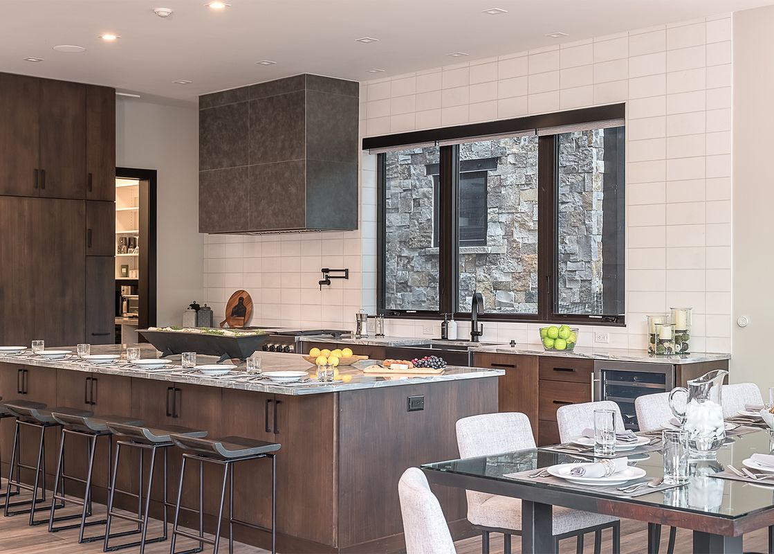 A modern kitchen and dining area in Triple 3 Lodge feature dark wood cabinetry, a large kitchen island with bar stools, and a glass dining table.