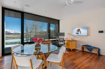 Modern study and dining area at The Dragonfly Lodge with a glass table, wooden desk, and a large window looking out onto snowy mountains.