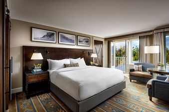 A spacious bedroom featuring a king-sized bed, dark wood furniture, and a private balcony overlooking a forested mountain landscape.