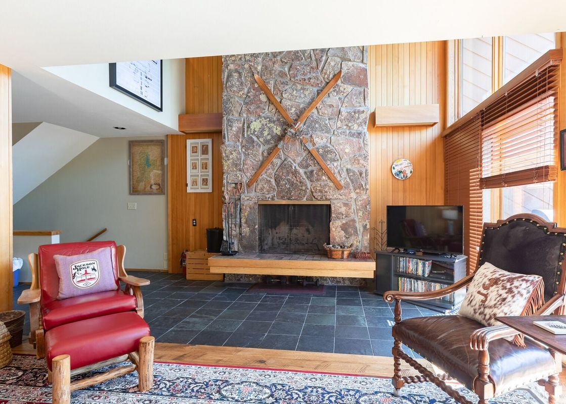 A cozy cabin-style living room at Windriver 12 featuring a stone fireplace, wood-paneled walls, and leather armchairs.