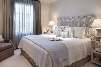 A serene bedroom at Lodge at Shooting Star 01 with a paisley upholstered headboard, white bedding, blue throw, and a window with sheer and opaque curtains.