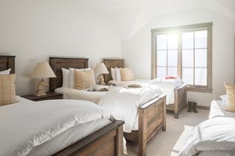 A bright bedroom in Four Pines 102 with three twin beds, wooden frames, white bedding, plaid pillows, horse-head lamps, and a large window with natural light.