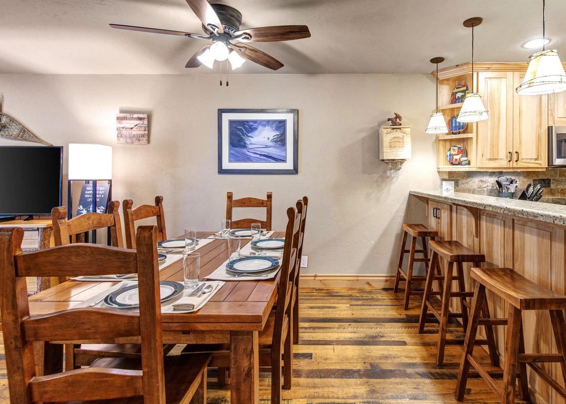 A cozy dining area at Snow Flower 132 Park City with a wooden dining table, chairs, and an adjacent kitchen bar with stools.