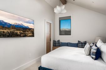 Bedroom at Moonlight Basin 9 Deep Forest Drive with a large TV, a king-sized bed with white linens and blue and white pillows, a window with a view of the mountains, and a wood-beamed ceiling.