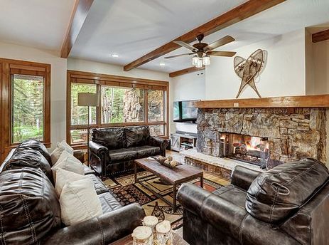 A cozy living room at Bear Paw Lodge 2 Bedroom features a stone fireplace, comfortable leather seating, and large windows with natural outdoor views.