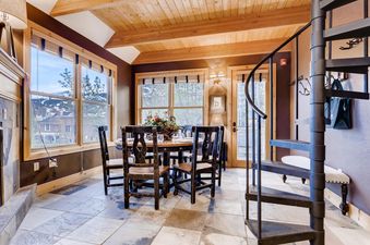 The dining area in Ridge Street Cottage features a round wooden table, chairs, a spiral staircase, and large windows with mountain views.