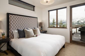 Bedroom with king-size bed, white linens, and a view of the mountains through a large window.