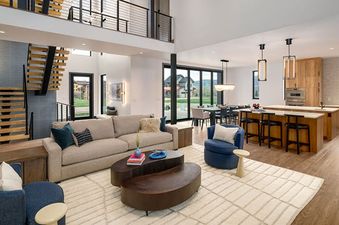 A high-angle view of the Wildhorse Preserve 6 Bedroom's open-concept living space, showing a modern living room, dining area, and kitchen with large windows and a stylish staircase.