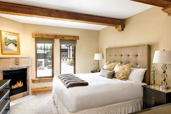 The bedroom at The Chateaux Four Bedroom Suite features a cozy fireplace, comfortable bed, and a pair of large windows overlooking a courtyard.