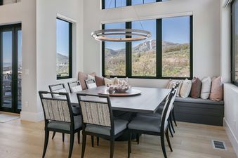 A spacious dining area at 11981 N Gemini Way SkyRidge with a dark wood table, eight chairs, a circular chandelier, and large windows offering mountain views.