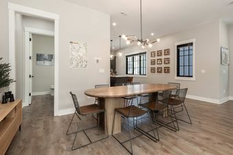 A dining room at Starview Chalet features a large oval wooden table with metal and leather chairs, illuminated by a modern chandelier and natural light from a large window.