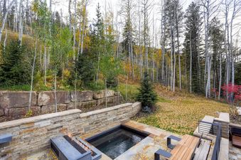 A luxurious outdoor hot tub and fire pit are nestled among autumn trees at Quantum, offering a serene woodland escape.