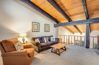 A cozy living area with a brown sofa, a patterned armchair, a wooden coffee table, and a vaulted wooden ceiling with exposed beams.