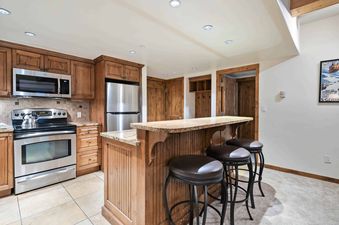 A kitchen with stainless steel appliances, wood cabinets, and a granite countertop.  The kitchen is open to a dining area with a bar.