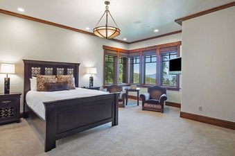 A luxurious bedroom at Solstice at Empire Pass features a dark wood bed, matching nightstands with lamps, and a corner seating area with large windows showcasing mountain views.