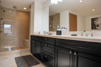 A modern bathroom with a dark wood vanity, dual sinks, a large mirror, and a glass-enclosed shower with tiled walls and a built-in bench.