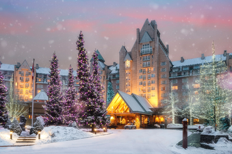 A luxurious hotel entrance at dusk, adorned with snow-covered Christmas trees featuring purple and white lights, creating a festive and inviting atmosphere.