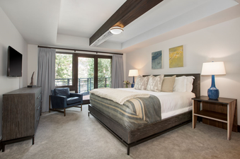 Bedroom in Lumiere Three Bedroom Unit 2 Bath featuring a king bed with pillows and a blanket. The bedroom has large windows with views of the trees outside.